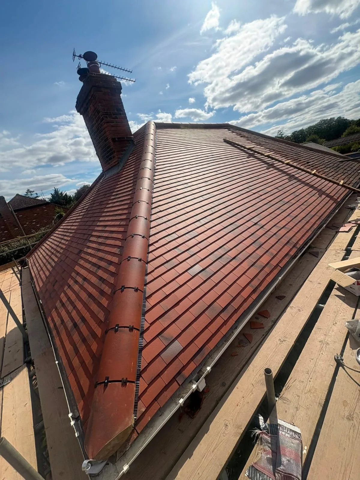Newly tiled hipped roof with a re-bedded ridge line and chimney against a blue sky